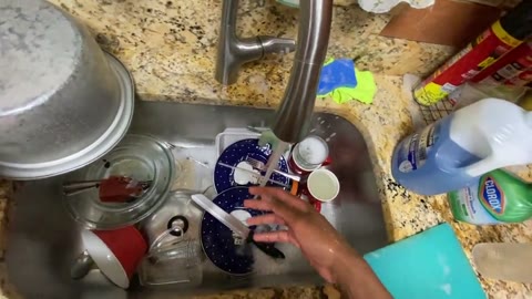 First-person video still of hands washing dishes in a home kitchen