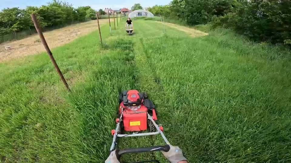 First-person video still of a lawn mower being pushed across a grassy yard