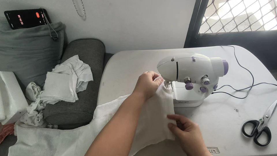 First-person video still of hands guiding fabric through a sewing machine